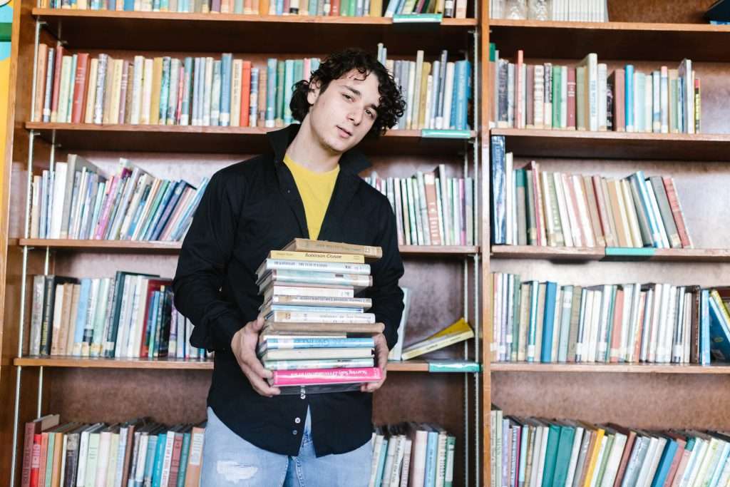 Young man holding a stack of books, symbolising the burden of study and registration costs.